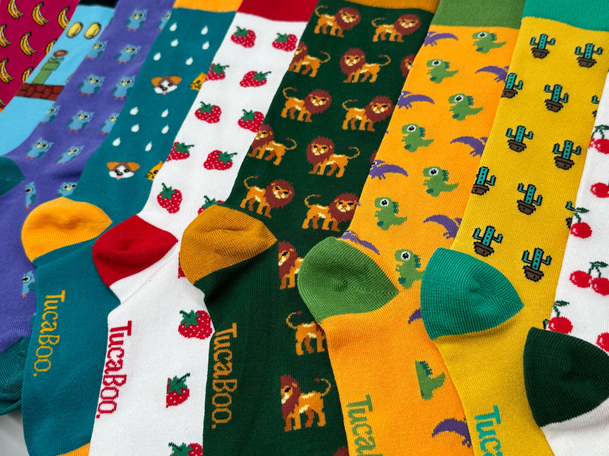 A row of colourful TucaBoo bamboo socks laid out in banana, lion, dinosaur, strawberry, cactus and cherry designs