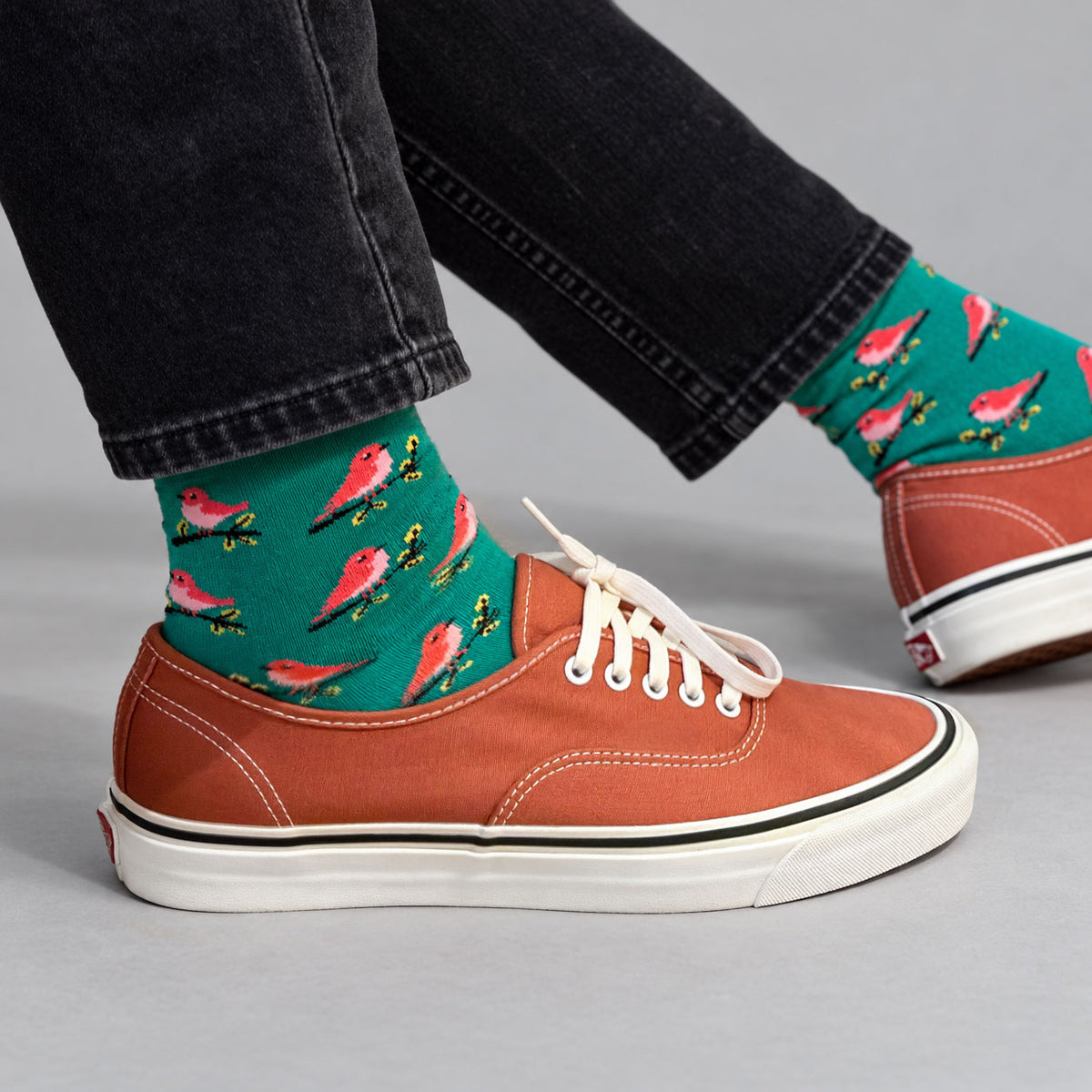 Green bamboo socks with a pink bird print, worn with black jeans and rust orange canvas trainers