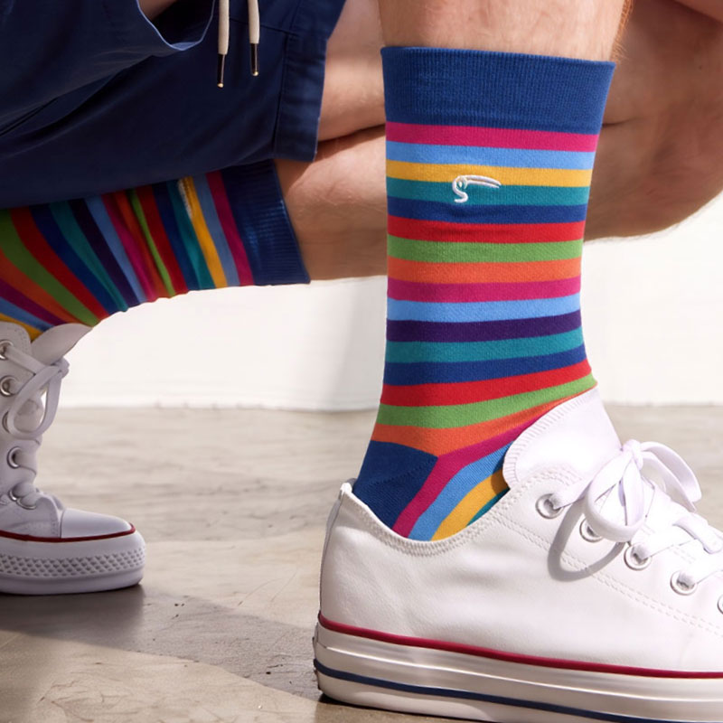 Multicoloured rainbow stripe bamboo socks with a navy cuff, worn with white canvas trainers